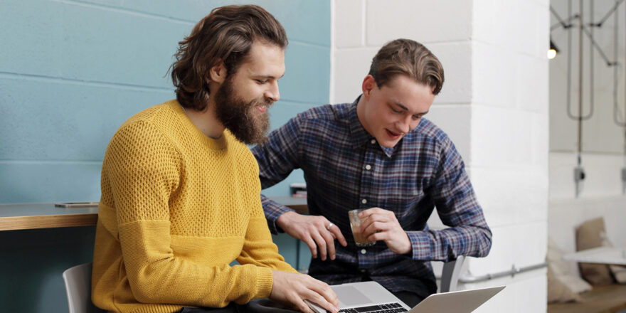 Two men research inflation on a laptop while sitting on bar stools