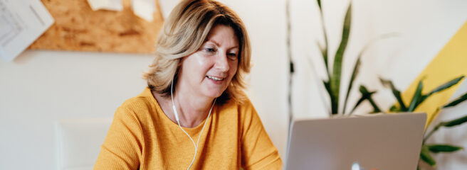 Woman in yellow shirt with headphones on and looking at her laptop.