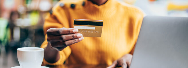 Woman in orange sweater holding a credit card and working on her laptop