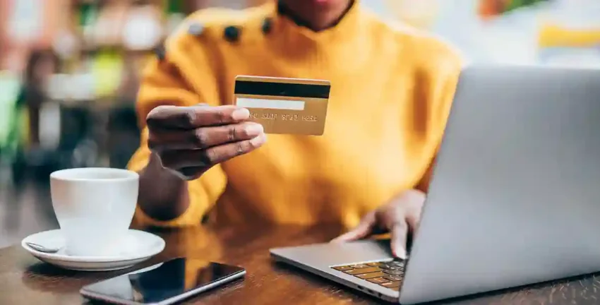 Woman in orange sweater holding a credit card and working on her laptop