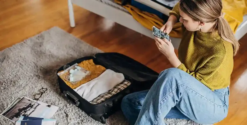 Woman researching vacation loans on her phone while packing a suitcase.