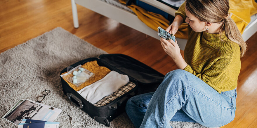 Woman researching vacation loans on her phone while packing a suitcase.