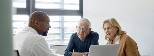 Man and woman sitting across a desk with a doctor as he talks to them