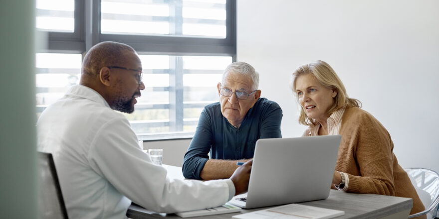 Man and woman sitting across a desk with a doctor as he talks to them