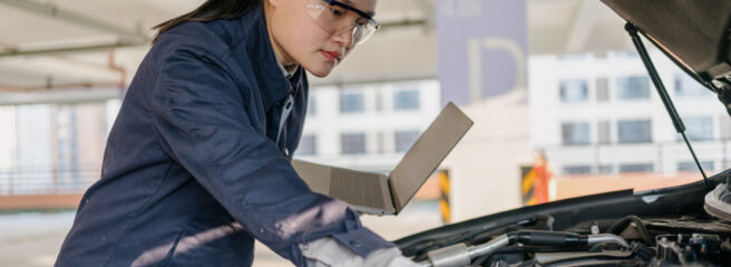 Mechanic in a blue jacket and goggles fixing something under the hood of a car