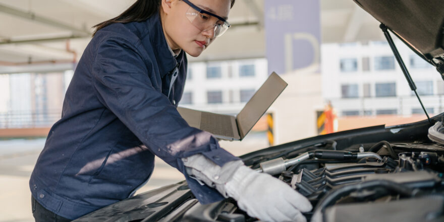 Mechanic in a blue jacket and goggles fixing something under the hood of a car