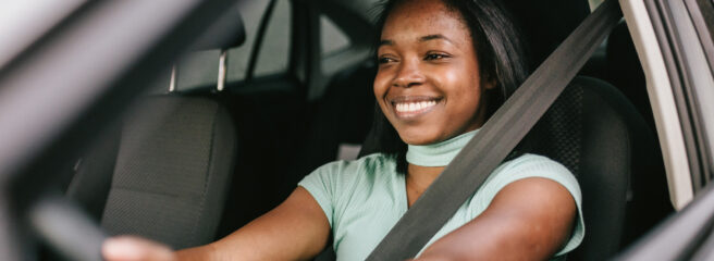 Woman sits behind the wheel of her car while considering refinancing her auto loan