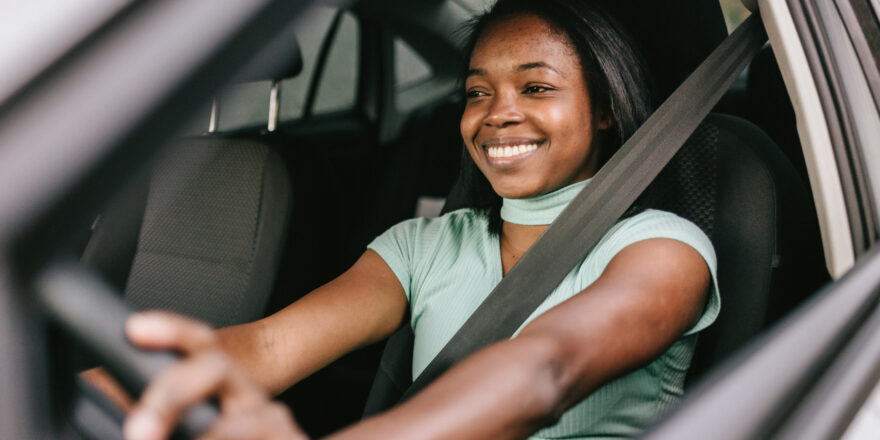 Woman sits behind the wheel of her car while considering refinancing her auto loan
