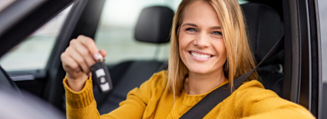 A woman holds the keys to her new car while sitting in the front seat