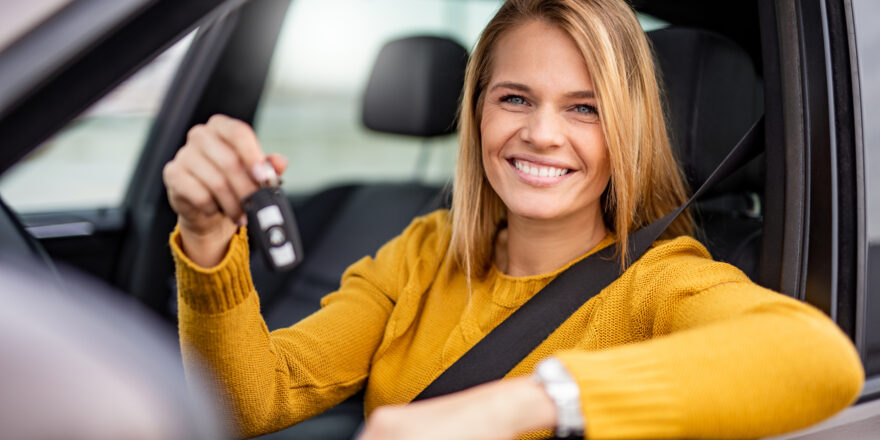 A woman holds the keys to her new car while sitting in the front seat