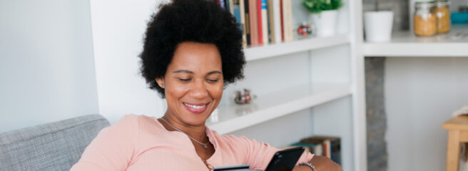 Woman sitting on couch holding her credit card and cell phone