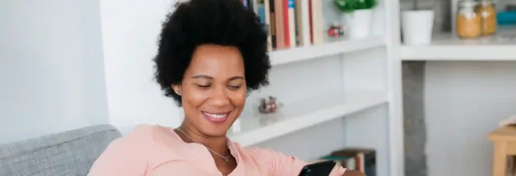 Woman sitting on couch holding her credit card and cell phone