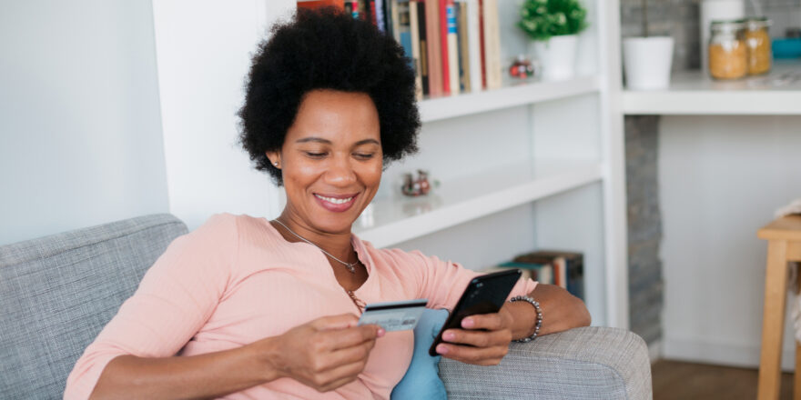 Woman sitting on couch holding her credit card and cell phone