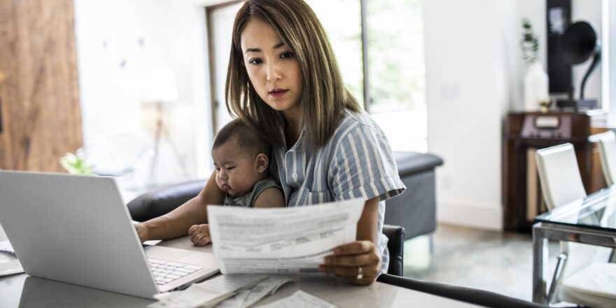 Woman with baby on her lap reviewing documents and working on laptop