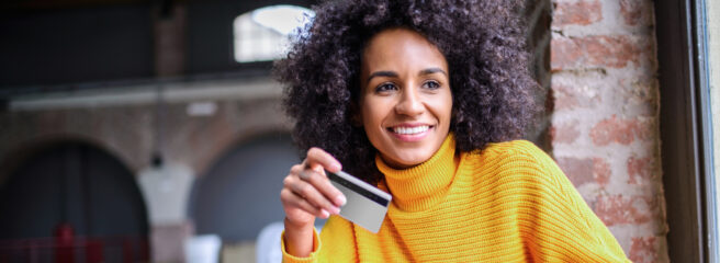 A woman in an orange sweater holding a notepad and credit card.