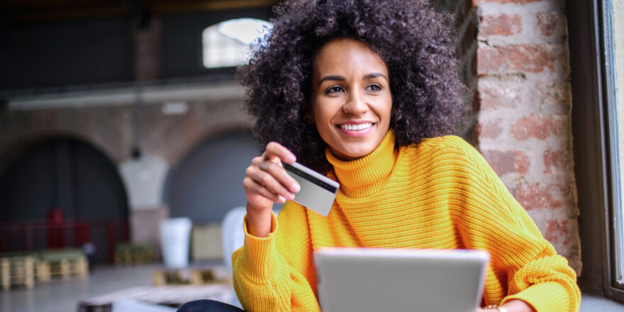 A woman in an orange sweater holding a notepad and credit card.