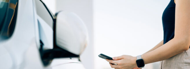 A woman uses her phone to research tips on refinancing a car loan with bad credit while standing next to her car