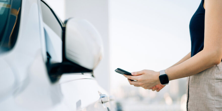 A woman uses her phone to research tips on refinancing a car loan with bad credit while standing next to her car