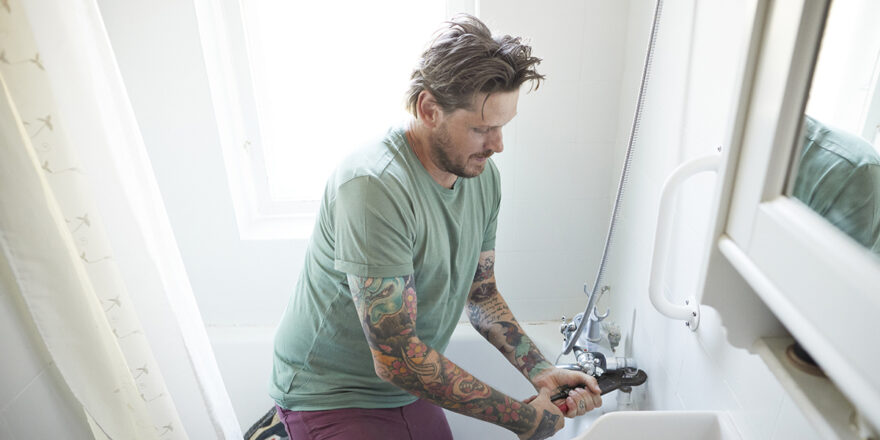 A man uses tools to work on a bathroom remodel in a house.