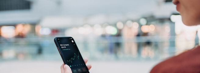 A person uses their cell phone to view the stock market and changes resulting from a bear market.