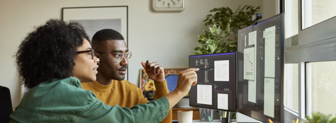 A woman and man look at multiple computer screens to research what loan amortization is.