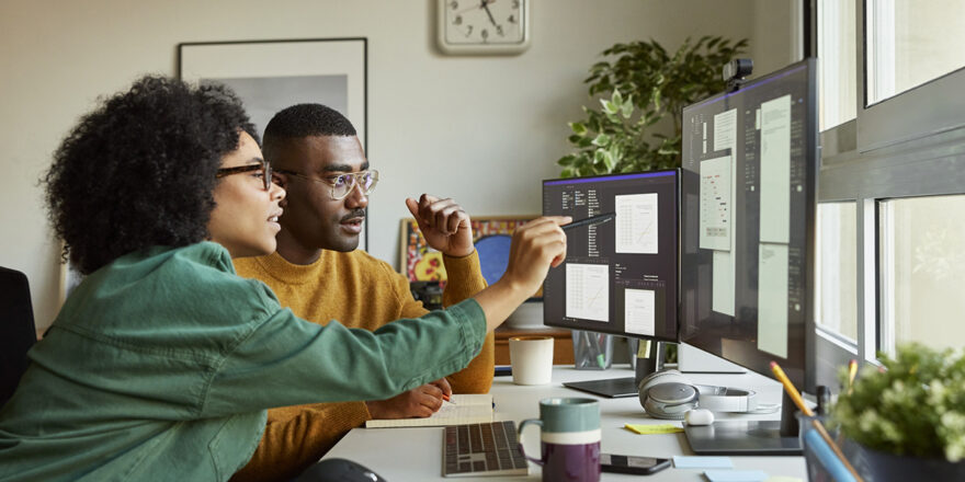 A woman and man look at multiple computer screens to research what loan amortization is.