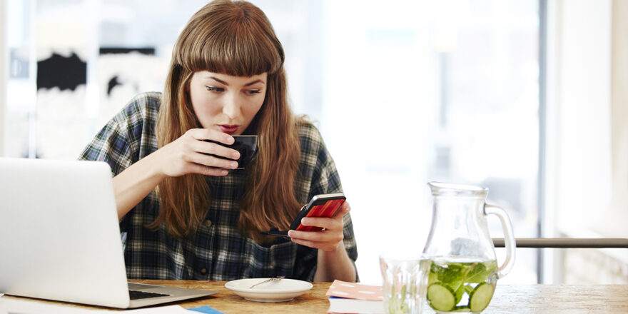 A young woman sips her drink while reading on her cell phone what a hard credit inquiry is.