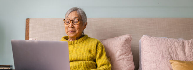 Elderly woman sitting on bed with laptop learning about interest