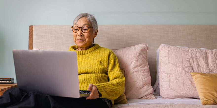 Elderly woman sitting on bed with laptop learning about interest