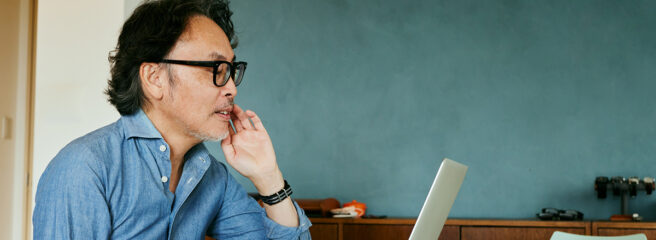 Senior man in denim shirt looking up sinking fund on computer