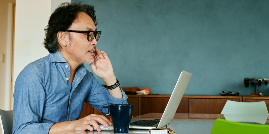 Senior man in denim shirt looking up sinking fund on computer