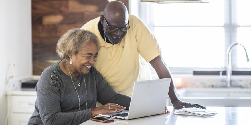 Senior couple in the kitchen looking at laptop about refinancing and credit