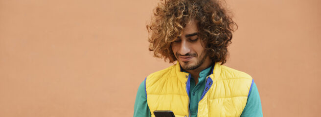 Young man with curly hair checking phone to learn about interest rate and APR