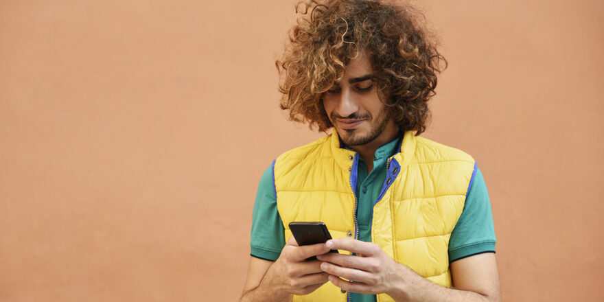 Young man with curly hair checking phone to learn about interest rate and APR