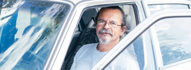 Senior man wearing glasses sitting in car with car door open