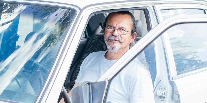 Senior man wearing glasses sitting in car with car door open