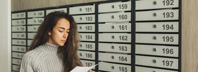 Young woman next to mailbox reading a letter about loan delinquency