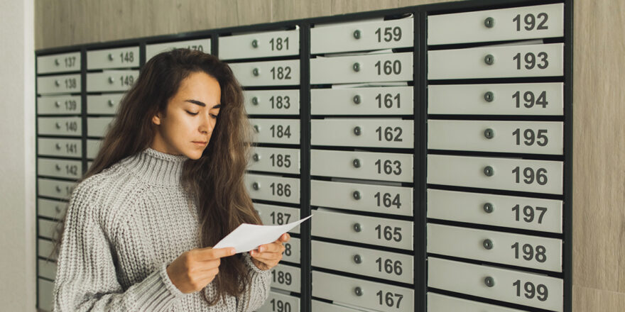 Young woman next to mailbox reading a letter about loan delinquency