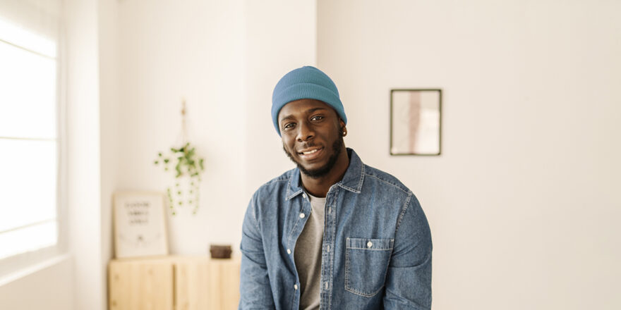 Close-up of a man in a home office with a teal beanie talking about a personal loan through Upstart