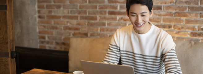 Young man in a black and white striped shirt using a laptop to learn about adverse action letter in a coffee shop