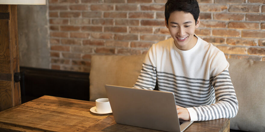 Young man in a black and white striped shirt using a laptop to learn about adverse action letter in a coffee shop