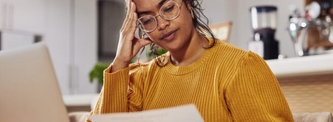 Young woman with white glasses at the dining table with open laptop thinking about the default on her loan