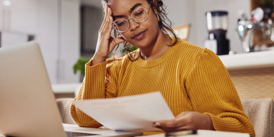 Young woman with white glasses at the dining table with open laptop thinking about the default on her loan