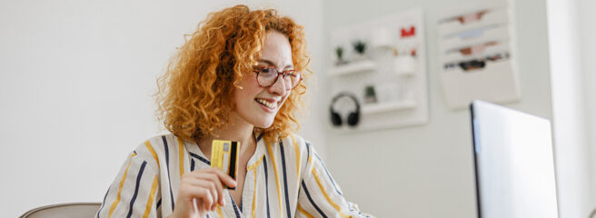 Young woman with curly red hair sitting at home office with laptop and credit card, learning about the 5 Cs of Credit