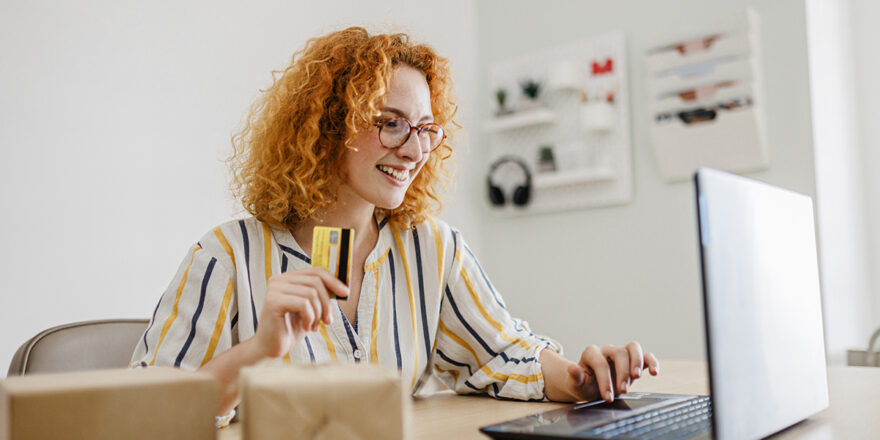 Young woman with curly red hair sitting at home office with laptop and credit card, learning about the 5 Cs of Credit
