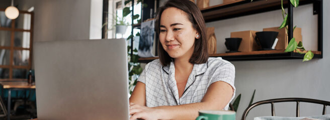 A young woman using a laptop in a cafe, learning about how to get a low interest personal loan