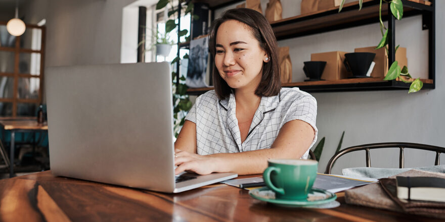 A young woman using a laptop in a cafe, learning about how to get a low interest personal loan