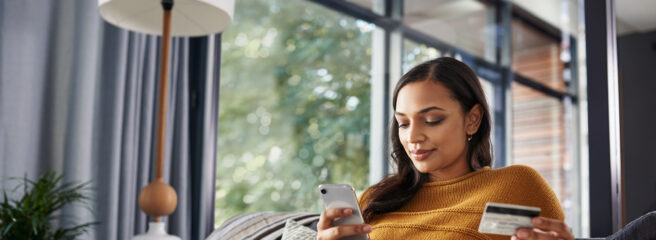 Shot of a young woman paying off her credit card debt while on a couch at home