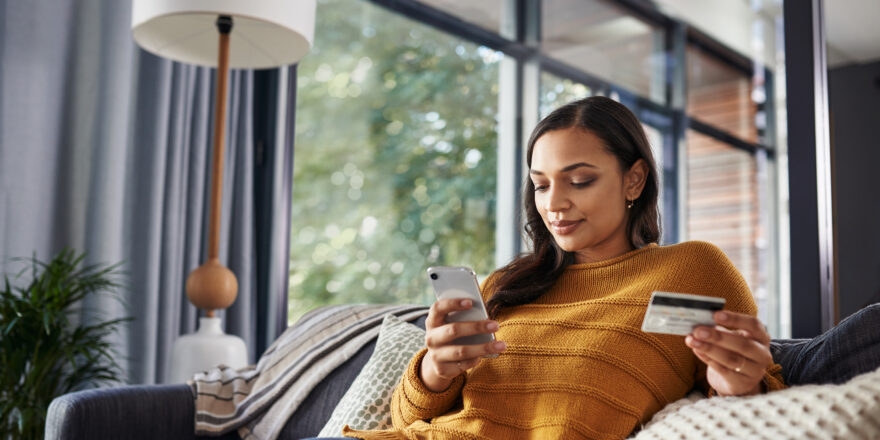 Shot of a young woman paying off her credit card debt while on a couch at home