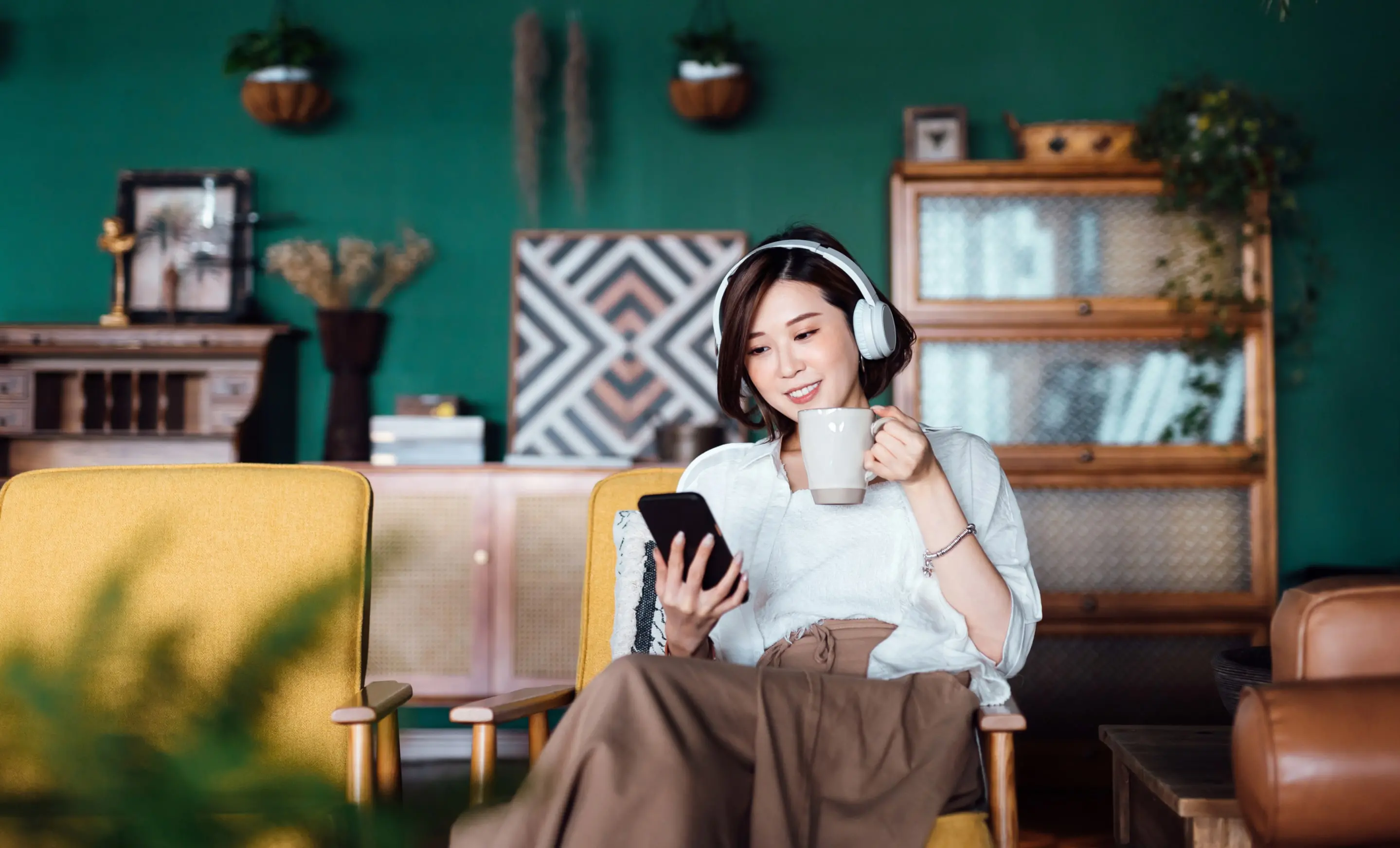 A young woman listens to a podcast about personal loans through Upstart on her smartphone while holding a cup of coffee.